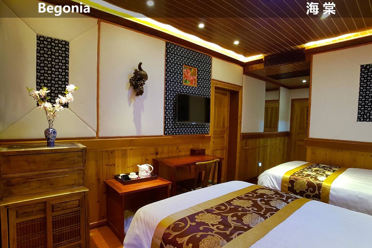 A hotel room with two beds, a wooden dresser, a small table with a tray of tea, and a vase with flowers.