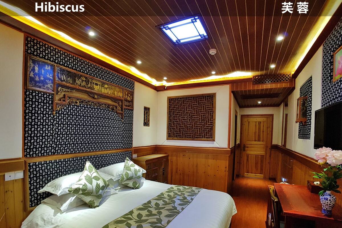 A hotel room with a bed, wooden paneling, a decorative wall, a ceiling light, and a TV.