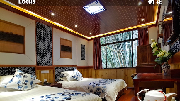Ett hotellrum med två sängar, träpanel på väggarna, ett stort fönster med utsikt över bambuskog och ett traditionellt teservis på ett träbord.