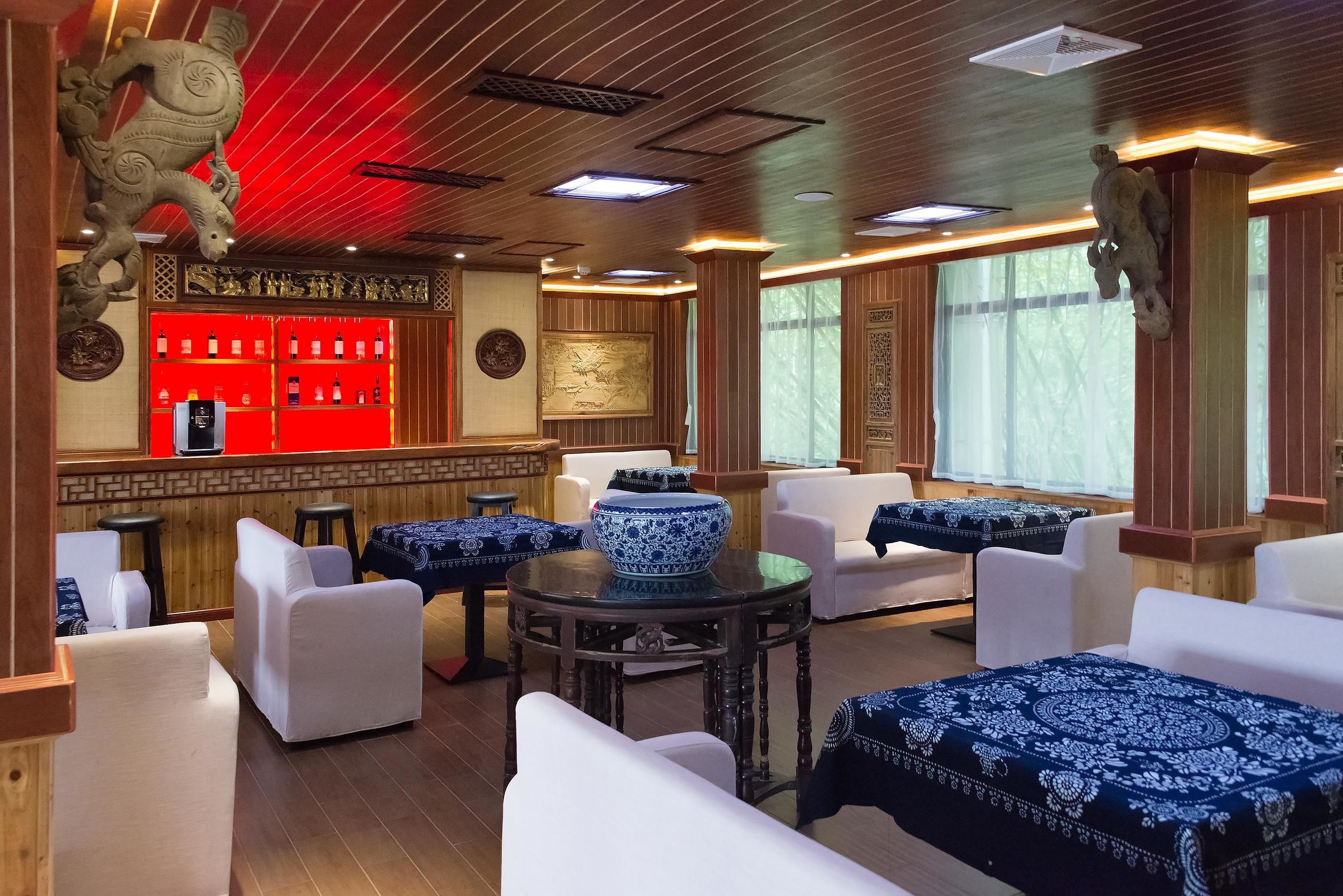 A traditional-style room with white sofas, a round table with a blue and white patterned tablecloth, and a red bar area with shelves of bottles.