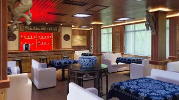 A traditional-style room with white sofas, a round table with a blue and white patterned tablecloth, and a red bar area with shelves of bottles.