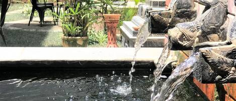 A small outdoor water feature with a stone sculpture, surrounded by potted plants and a brick wall.