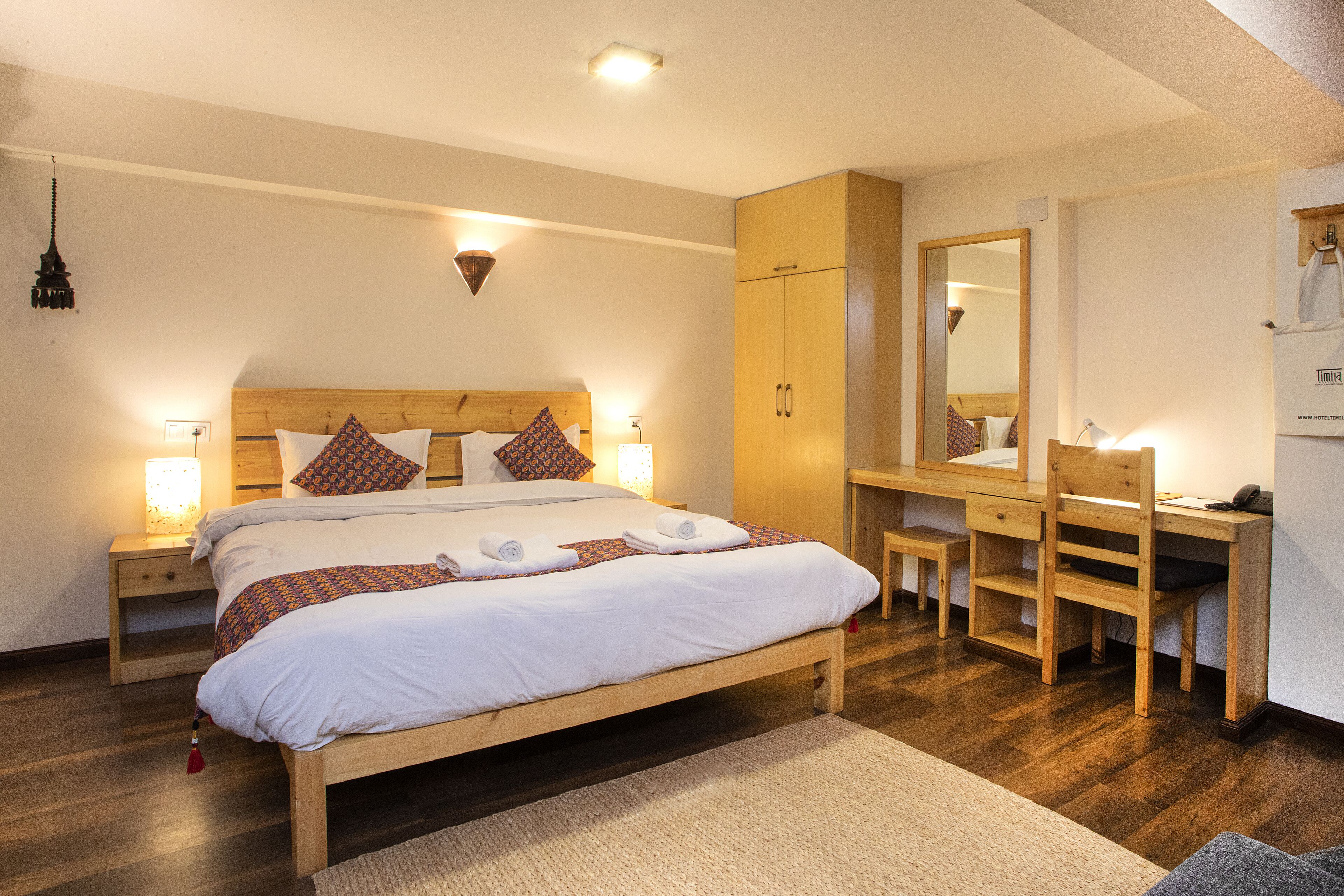 A bedroom with a wooden bed, bedside tables with lamps, a wooden desk, and a mirror.