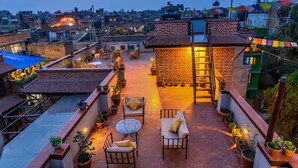 A rooftop terrace with outdoor seating, potted plants, and a brick wall structure.