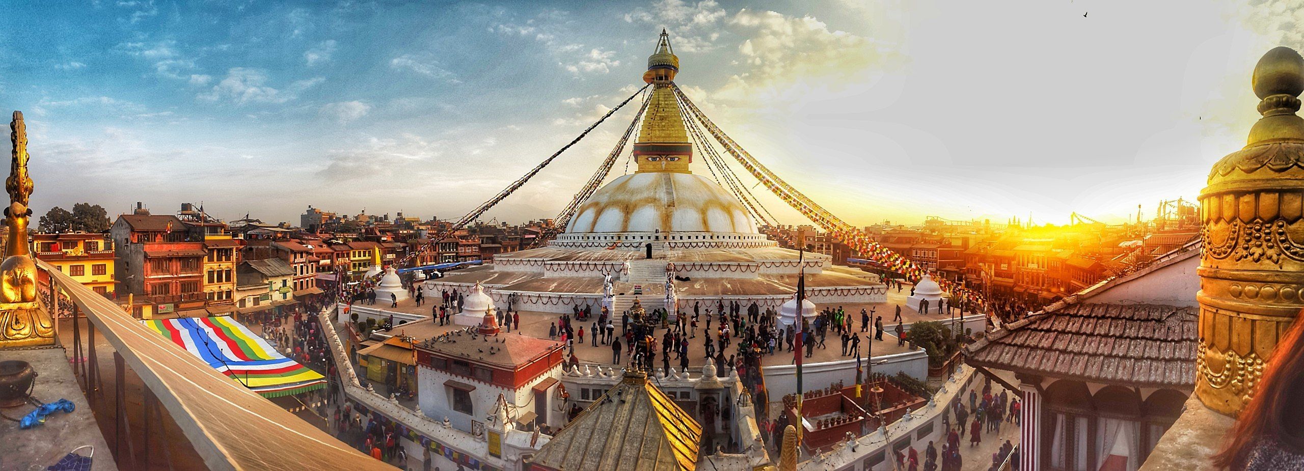 A large, white, domed structure with a golden spire, surrounded by a bustling square with people and traditional buildings.