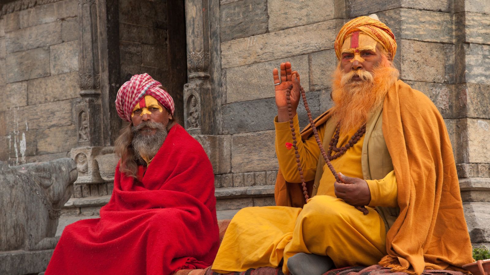 Two individuals seated in front of a stone building with intricate carvings.