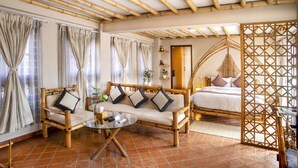 A room with a bamboo ceiling, a sofa with cushions, a glass coffee table, and a bed with pillows.