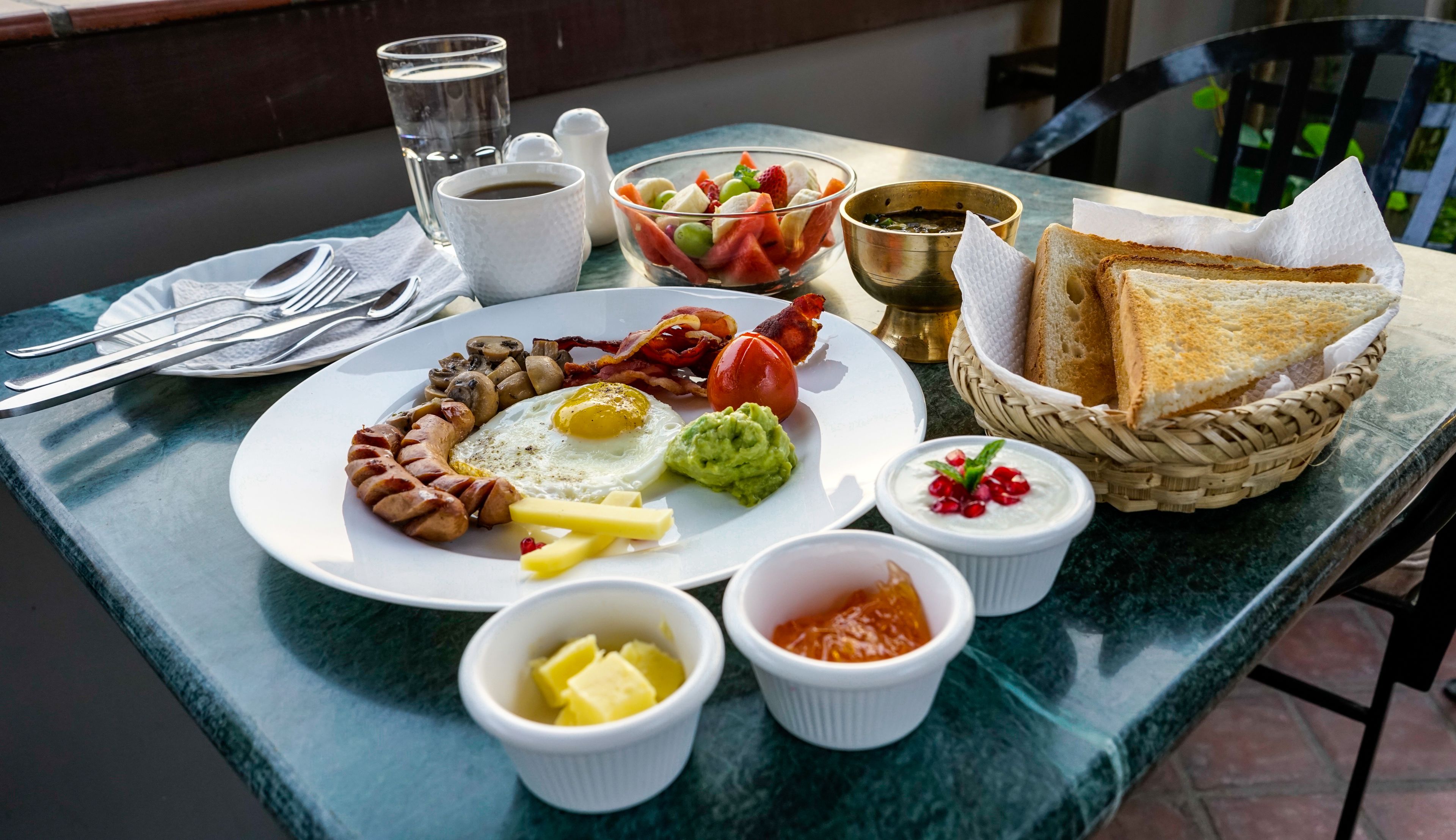 Ein Frühstücksteller mit Eiern, Speck, Würstchen und Toast auf einem Tisch.