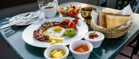 Ein Frühstücksteller mit Eiern, Speck, Würstchen und Toast auf einem Tisch.