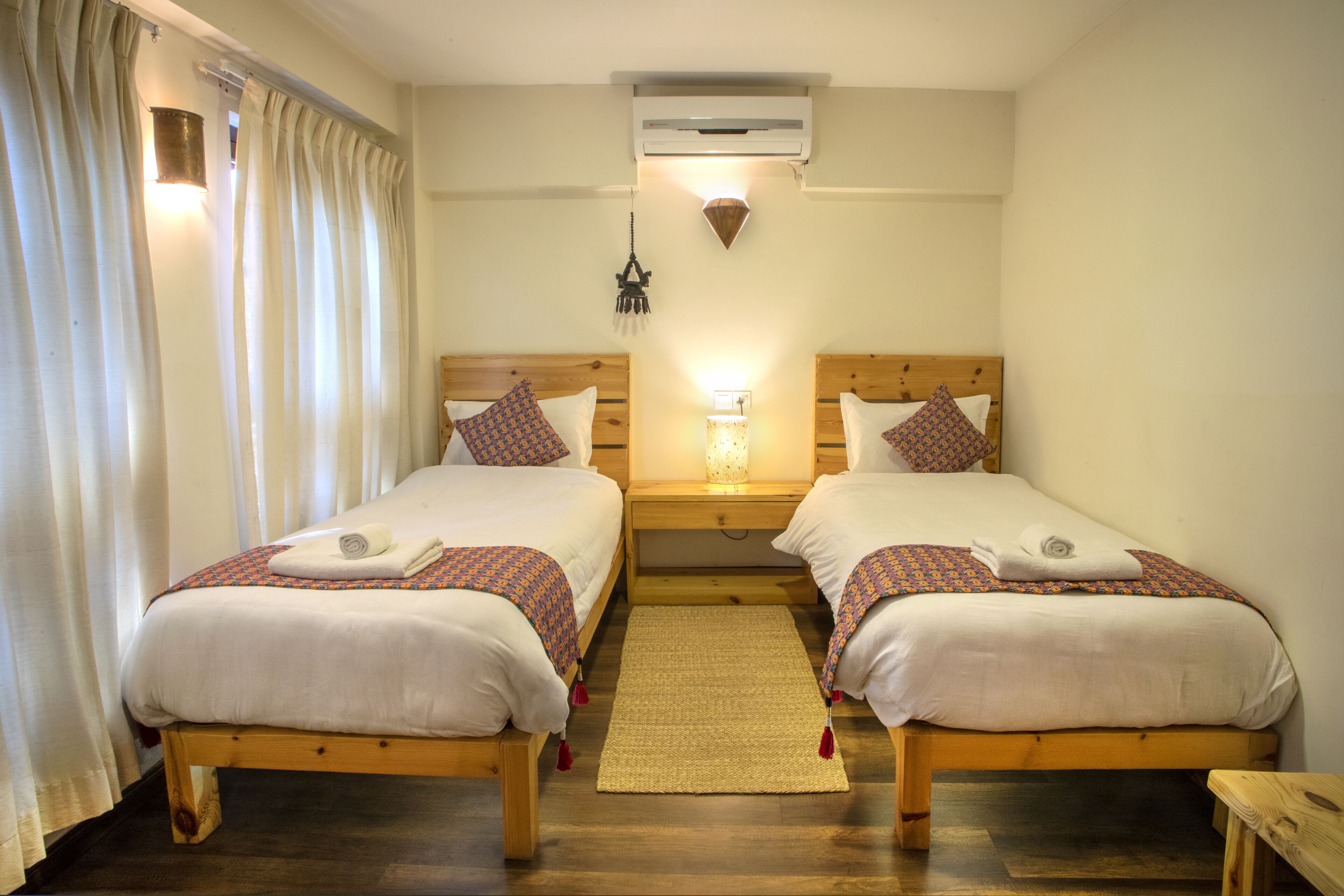 A double room with two beds, a wooden headboard, a small rug, and a wall-mounted air conditioner.