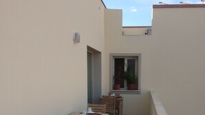 A row of wooden tables and chairs on a tiled patio with a small window and potted plants. - La Casa di Pier (Olbia)