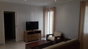A living room with a television on a wooden stand, a sofa, a coffee table, and a window with curtains. - La Casa di Pier (Olbia)