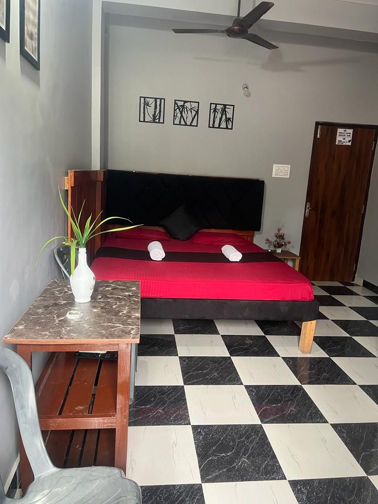 A room with a bed, a table with a plant, a chair, and a checkered floor.