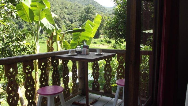 Eine Holzterrasse mit Tisch und zwei Stühlen, die auf eine üppige grüne Landschaft mit Hügeln im Hintergrund blickt.