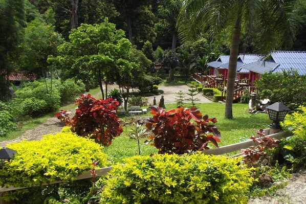 A lush garden with a variety of plants and trees, a wooden fence, and a small building with a blue roof.