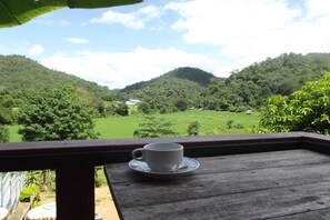 A wooden table with a white cup and saucer on it, overlooking a lush green valley with hills and a clear sky.