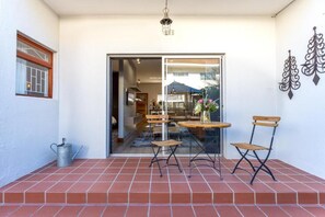 A patio with a table and chairs, a metal watering can, and a sliding glass door leading to an interior space. - Avemore Vredehof No 3 (Stellenbosch)