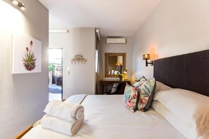 A hotel room with a bed, a wall-mounted air conditioner, a mirror, and a wall-mounted light fixture. - Avemore Vredehof No 3 (Stellenbosch)