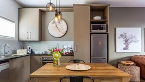 A modern kitchen with a wooden dining table, pendant lights, a clock, and a refrigerator.