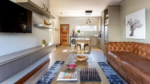 A modern living room with a leather sofa, a coffee table with magazines, and a kitchen in the background.