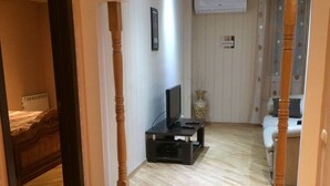 A room with wooden flooring, a television on a stand, a bed with a headboard, and a door leading to another room. - Bachos Apartment (Tbilisi)