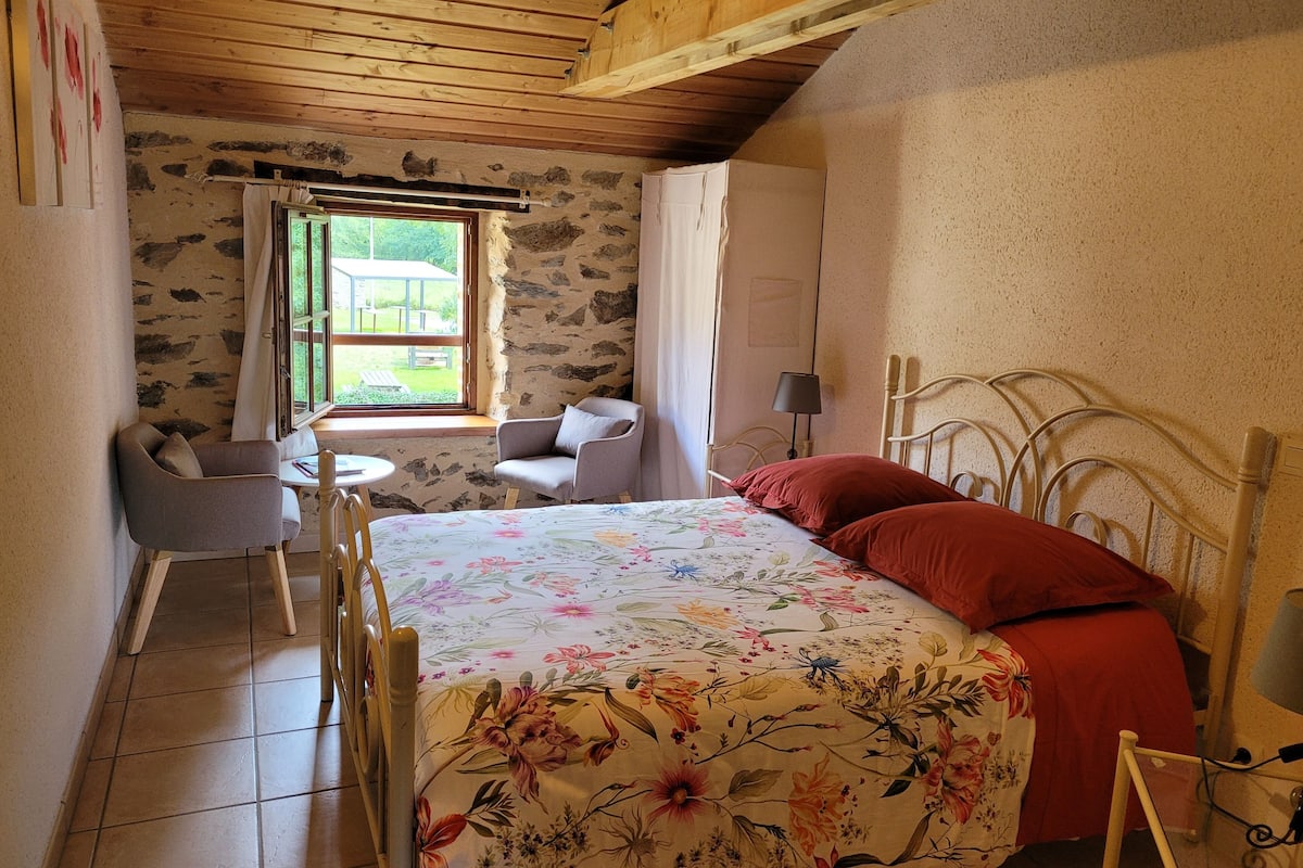 Une chambre à coucher avec un lit, une chaise, une petite table et une fenêtre avec des rideaux.