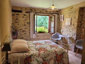 Relax in this charming room with a large bed, small dining table, and a view of lush greenery.