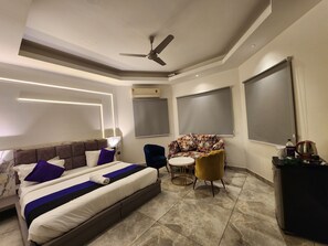 Ein modernes Hotelzimmer mit einem großen Bett, einem Deckenventilator, einem runden Tisch und einem kleinen Schreibtisch mit Wasserkocher.