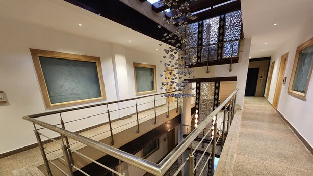 Um interior em vários níveis, com uma escadaria central, guarda-corpos de vidro e luminárias decorativas.