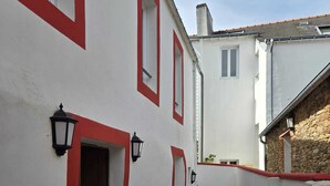 A narrow courtyard with a white building featuring red trim, a small table with chairs, and a potted plant. - Hotel Le Saint Amant (Le Palais)