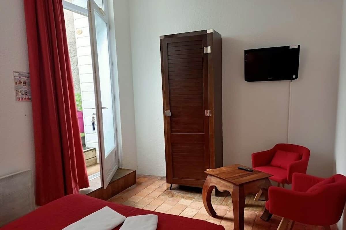 Ein Hotelzimmer mit einem Bett, einem Holzschrank, einem kleinen Tisch, zwei roten Stühlen und einem Fernseher an der Wand.