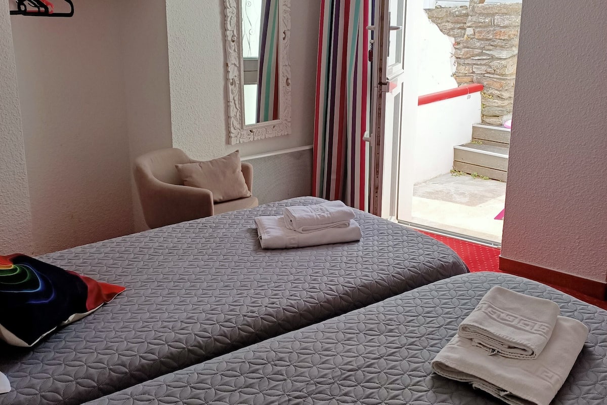 Ein Hotelzimmer mit zwei Betten, einem Sessel, einem Spiegel und einem Fenster mit Vorhängen.