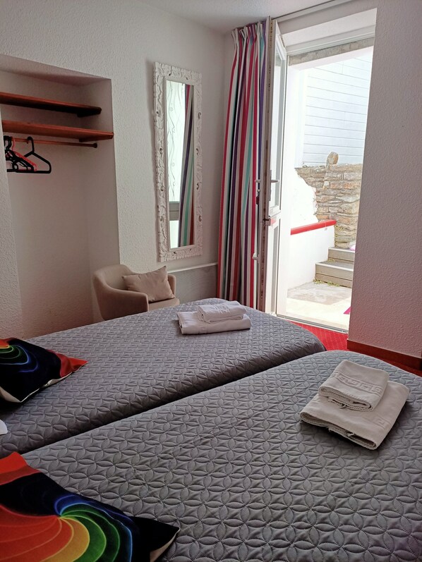 Habitación de hotel con dos camas, una silla, un espejo y un ventanal con cortinas.