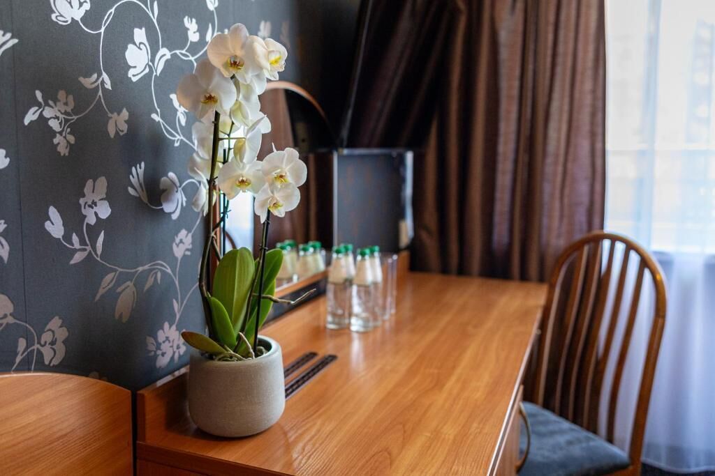A dining table with a potted orchid, a bottle of water, and a glass of water on it.