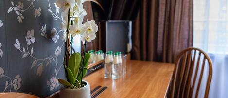 A dining table with a potted orchid, a bottle of water, and a glass of water on it.