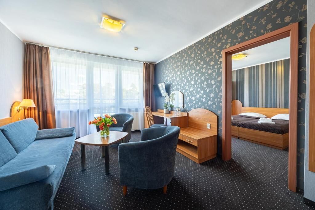 A hotel room with a sofa, a small table with flowers, a desk, a bed, and a mirror.