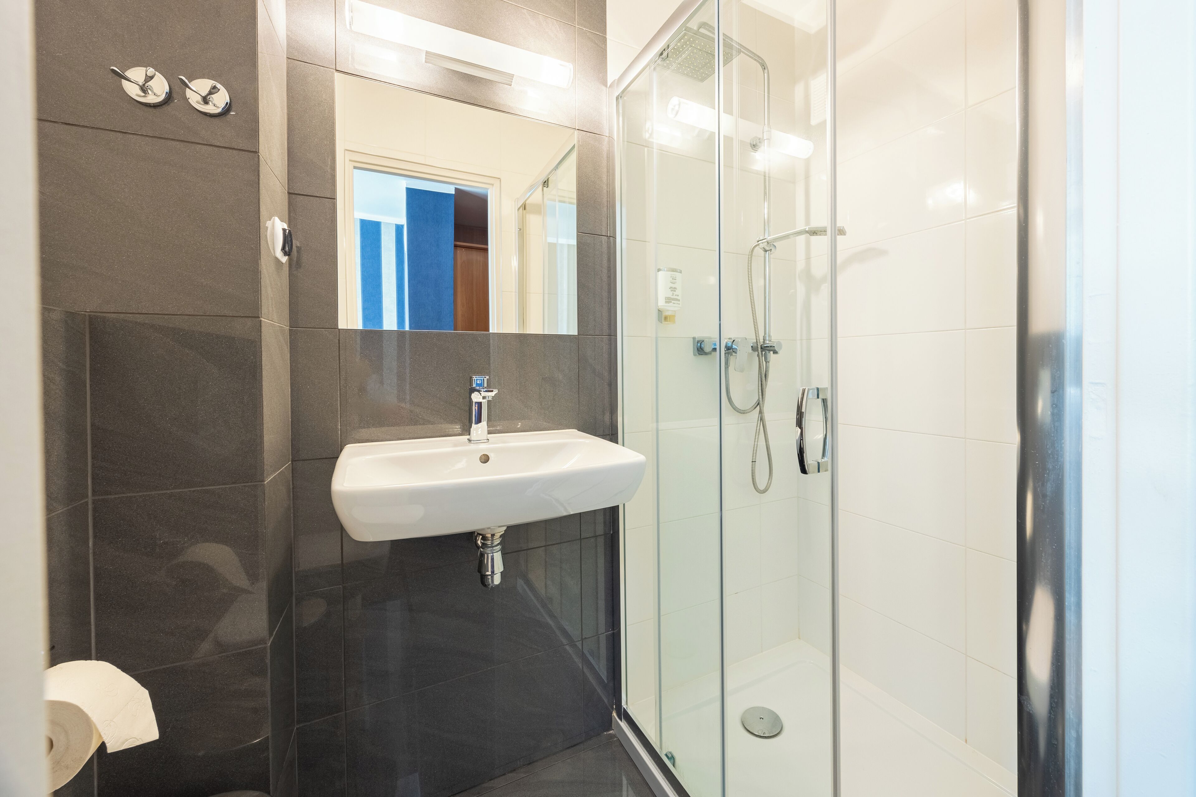 A modern bathroom with a glass-enclosed shower, a white sink, and dark tiled walls.