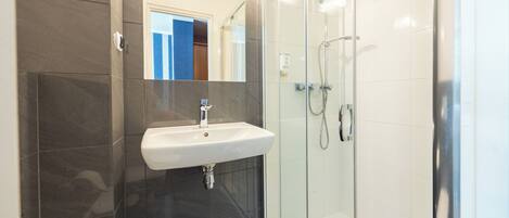 A modern bathroom with a glass-enclosed shower, a white sink, and dark tiled walls.