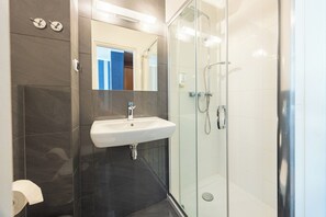 A modern bathroom with a glass-enclosed shower, a white sink, and dark tiled walls.