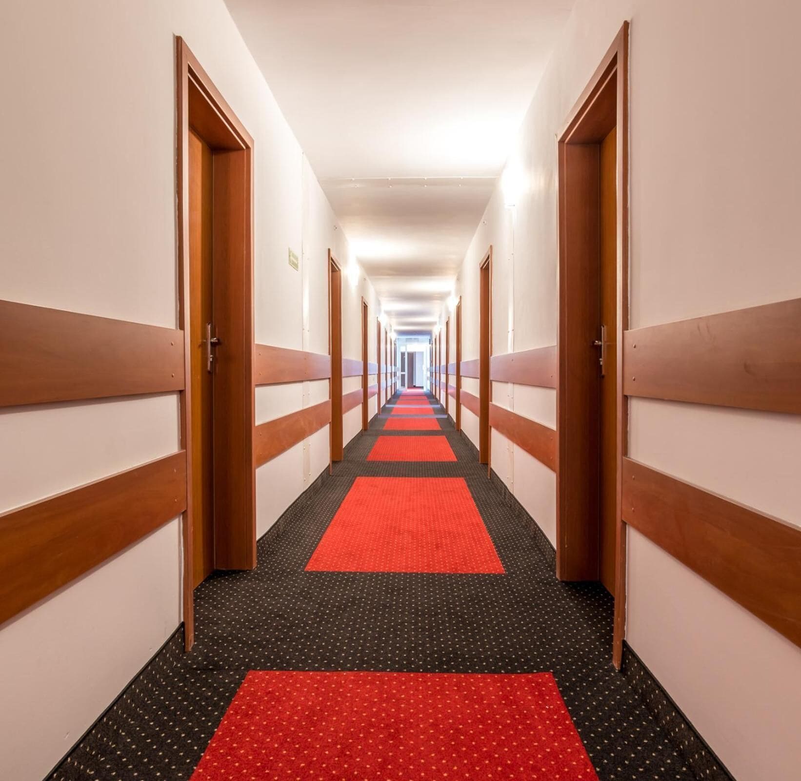 Un pasillo de hotel con puertas de madera, una alfombra roja y un suelo con estampado rojo y negro.