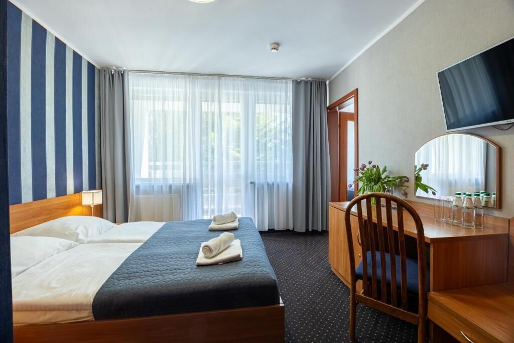 A hotel room with a bed, a desk, a chair, a television, and a window with curtains.