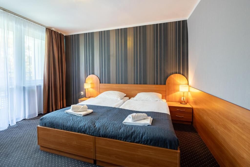 Een hotelkamer met een groot bed, twee bedlampen, een houten hoofdeinde en uitzicht op het landschap door het raam.