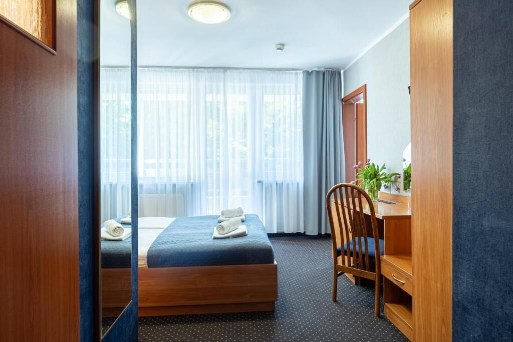 A hotel room with two beds, a desk, a chair, and a large window with curtains.