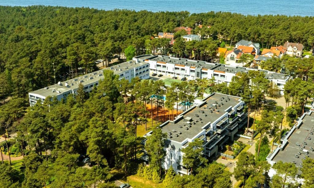 Una vista aerea di un complesso alberghiero circondato da una fitta foresta, con diversi edifici e un'area di parcheggio.