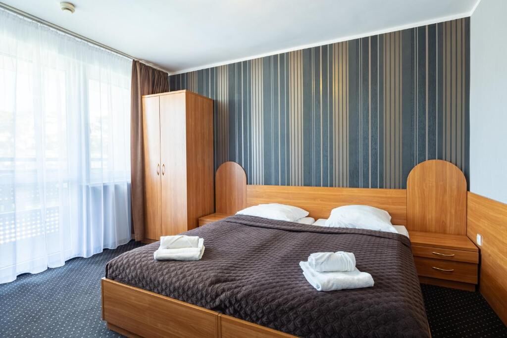 A hotel room with a large bed, wooden headboard, a wardrobe, and a window with curtains.