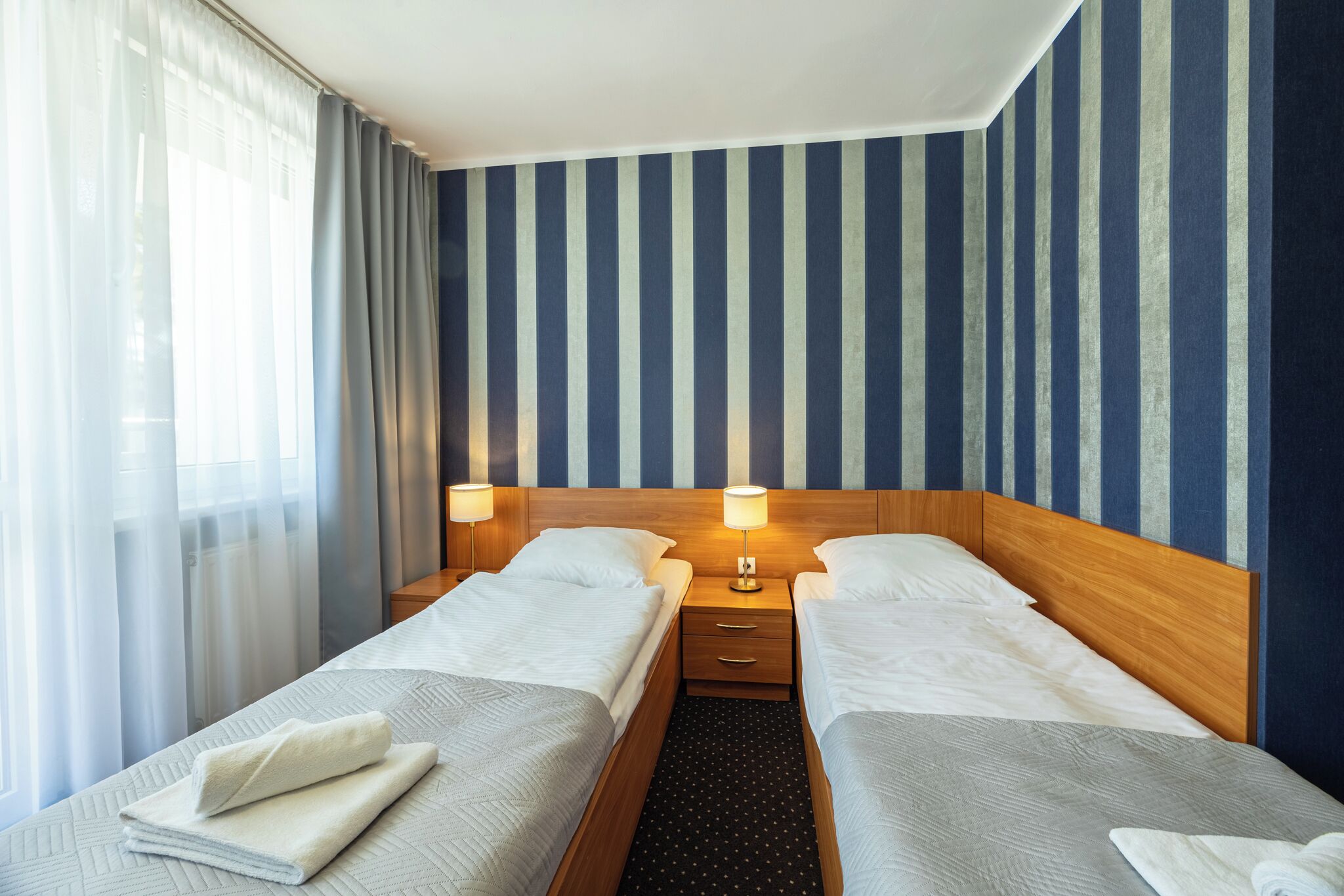A hotel room with two beds, a wooden headboard, and a striped wall.