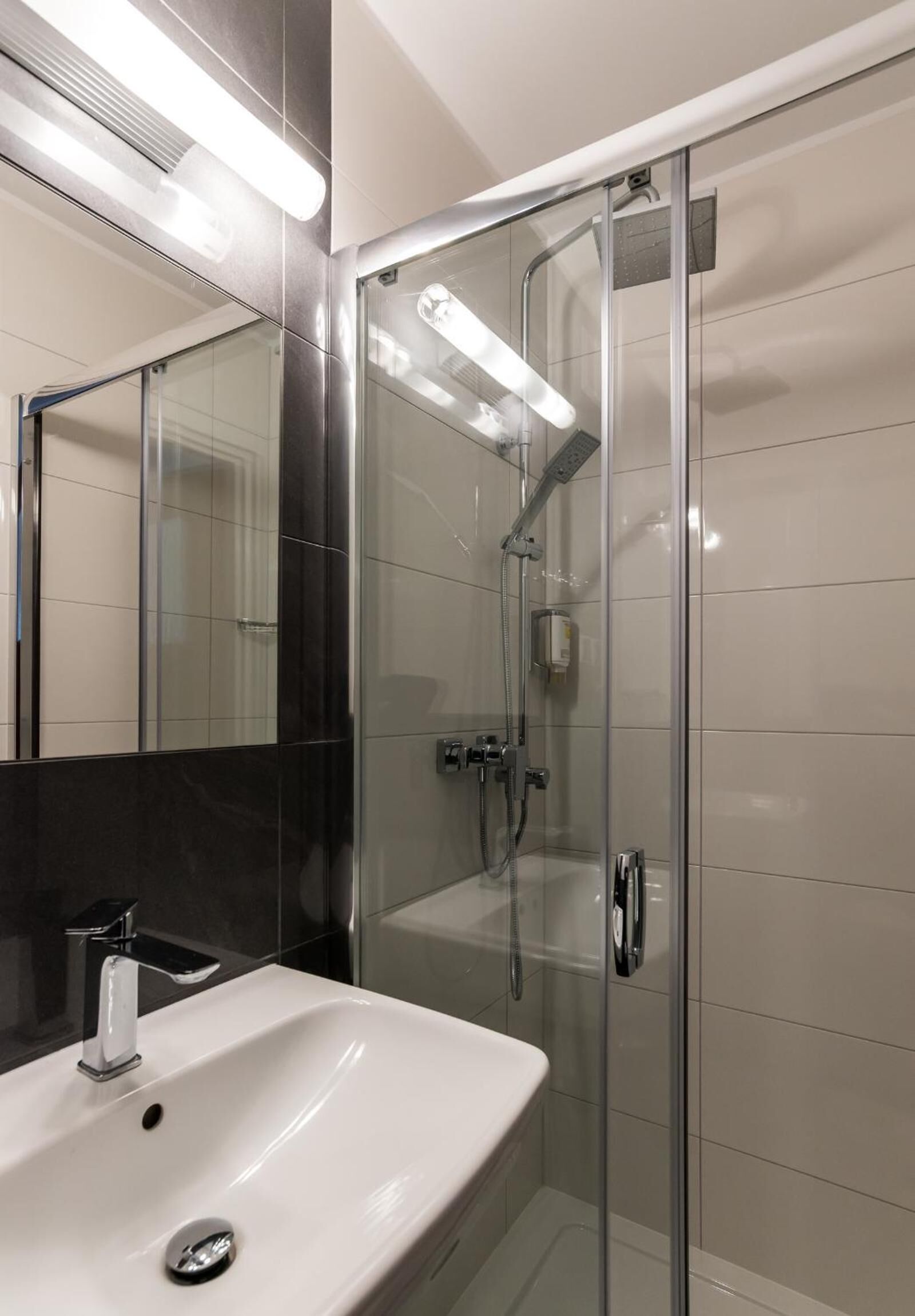 A modern bathroom with a glass-enclosed shower, a white sink, and a large mirror.