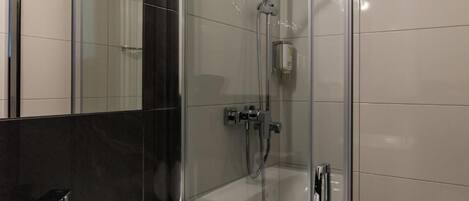Un baño moderno con ducha acristalada, lavamanos blanco y un espejo grande.