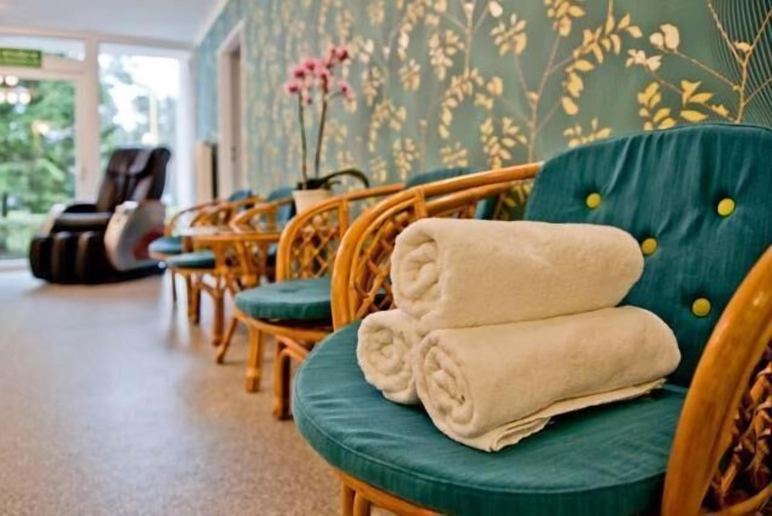 Una hilera de sillas de mimbre con cojines azul turquesa y toallas blancas enrolladas, en una habitación con papel tapiz floral y vistas a espacios verdes al exterior.