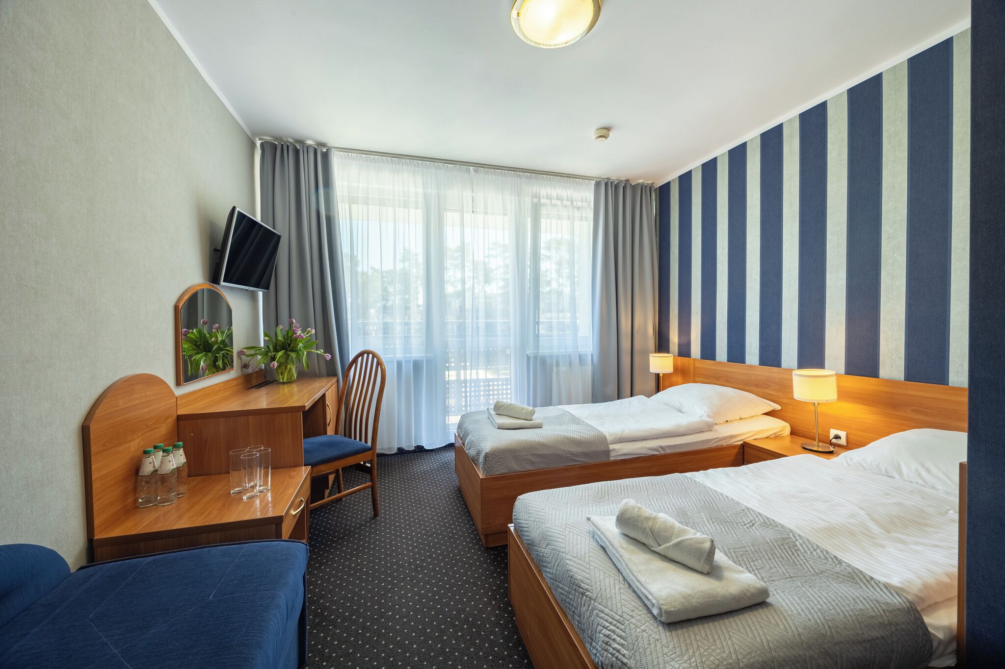 A hotel room with two beds, a desk with a TV, a chair, and a window with curtains.